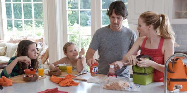 Maude Apatow, Iris Apatow, Paul Rudd, and Leslie Mann stand around a kitchen counter eating.