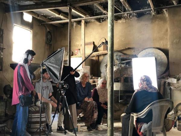 A group of people sit for an interview. Other people with camera and lighting equipment stand around.