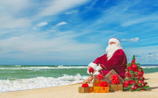 Santa Claus at sea beach with many gifts and decorated christmas tree - happy new year concept